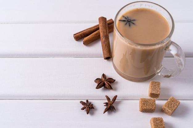 Masala chai thee in een mok, bruine suiker, kaneelstokjes en anijs over witte tafel.