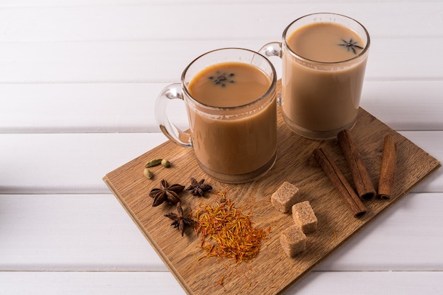 Masala chai thee in mokken, bruine suiker, kaneelstokjes, anijs en badian op witte tafel achtergrond.