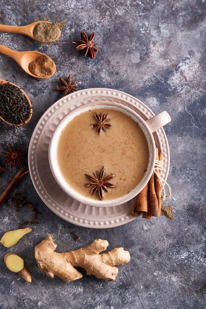 Masala tea in cup with spices ginger, cinnamon, anise, black pepper on gray sone table