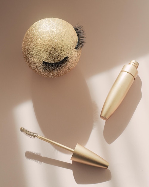 Mascara and a golden Christmas ball with false eyelashes The concept of festive makeup for women