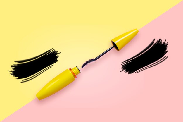 Mascara in tubo giallo con pennello aperto su occhiali da sole rosa e gialli con ciglia finte.