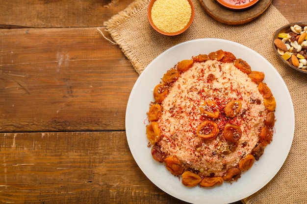 Masfouf van couscous met gedroogde vruchten in een groot bord op een houten tafel naast saffraan