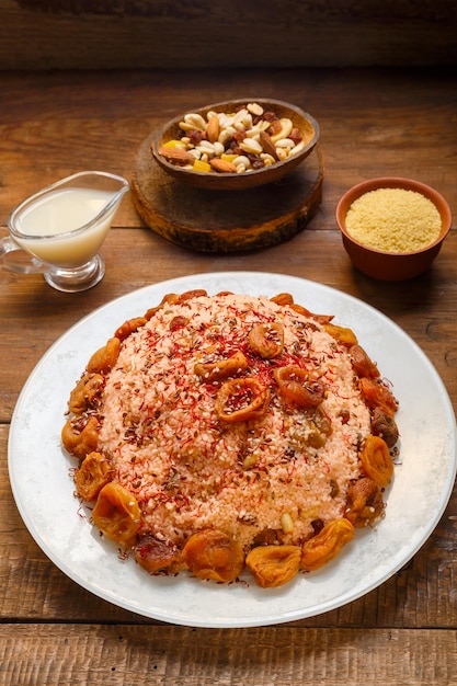 Masfouf van couscous op amandelmelk met gedroogde vruchten en noten op een houten tafel naast saffraan