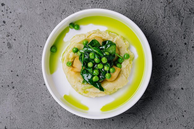 Mashed potato with butter green peas basil in a white bowl