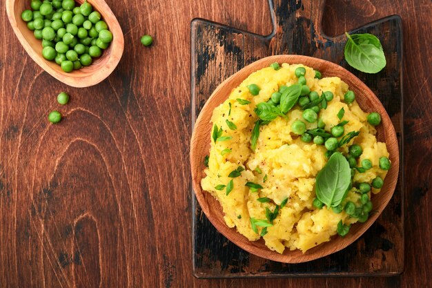 Mashed potato with butter, green peas, onions, basil on a rustic wooden background. Top view with close up.