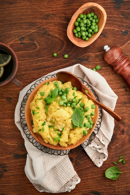 Mashed potato with butter, green peas, onions, basil in a white bowl