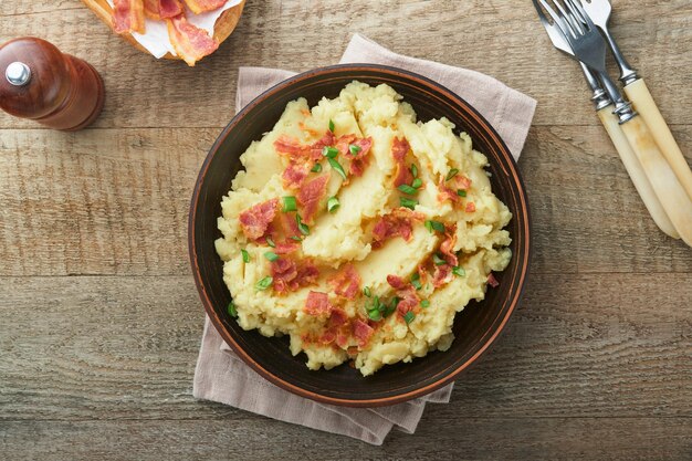 Foto purè di patate purè di patate al bacon con cipolla verde pepe e formaggio cheddar in ciotola su vecchi sfondi di legno delizioso purè di patate cremoso vista dall'alto