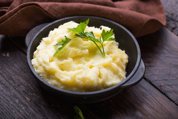 Mashed potatoes or boiled puree with parsley  in cast iron pot on dark wooden rustic .  top view