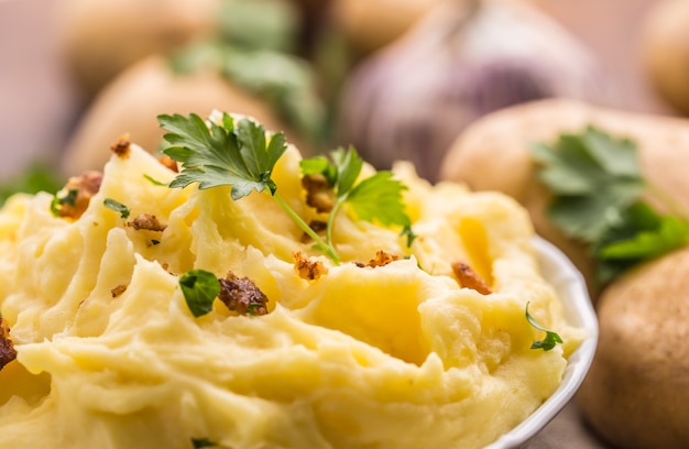 Mashed potatoes in bowl decorated parsley herbs and roasted bacon pieces.