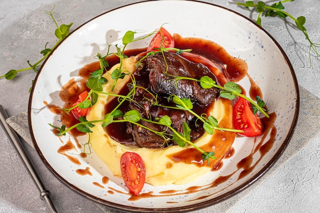 Photo mashed potatoes with beef in sweet and sour sauce decorated with tomatoes and microgreens