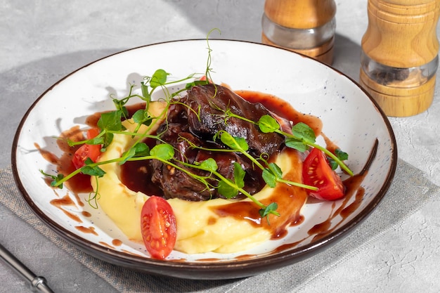 Mashed potatoes with beef in sweet and sour sauce decorated with tomatoes and microgreens