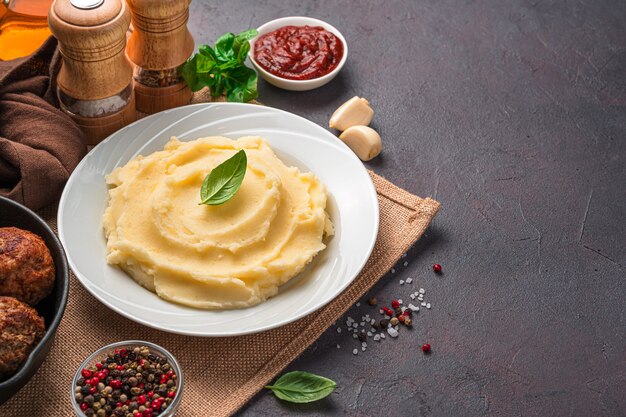 Mashed potatoes with fresh basil on a brown background. Garnish. Side view, copy space.