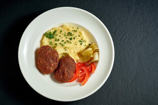 Mashed potatoes with Kiev cutlets in a white plate on a black background. Chicken kiev