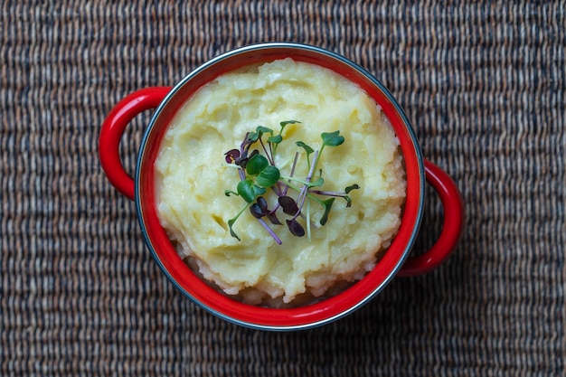 Mashed potatoes with radish microgreens in a red saucepan close up top view