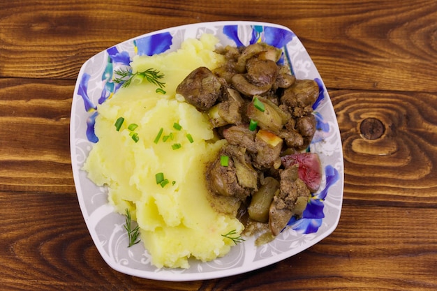 Mashed potatoes with stewed chicken liver with apple and onion on wooden table