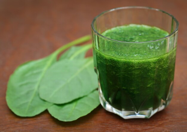 Mashed spinach smoothie in a glass on wooden surface