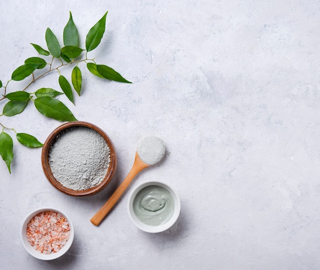 Maschera fatta di argilla verde cosmetica a casa in una ciotola di legno e sale marino rosa su un fondo concreto grigio. il mio cosmetologo