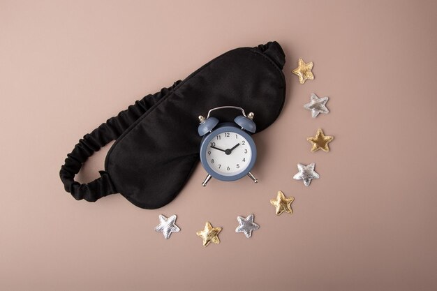 Mask for sleep and alarm on the pastel background.Golden and silver stars around.Circadian rhythms and healthy sleep concept.Vertical photography.