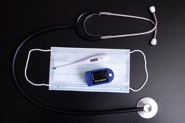 Mask stethoscope thermometer and oximeter on black background