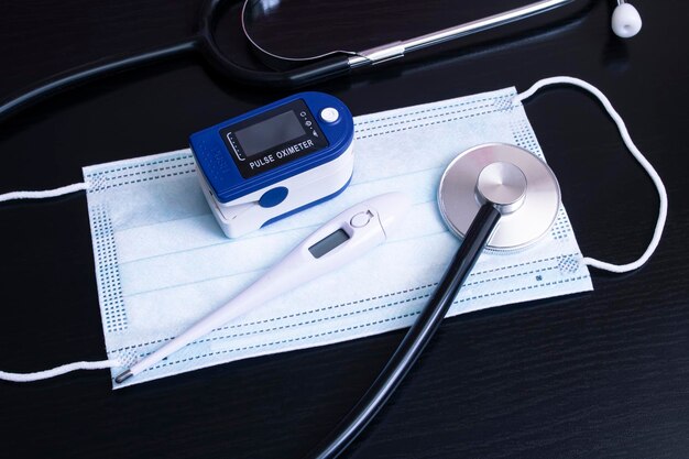 Mask stethoscope thermometer and oximeter on black background