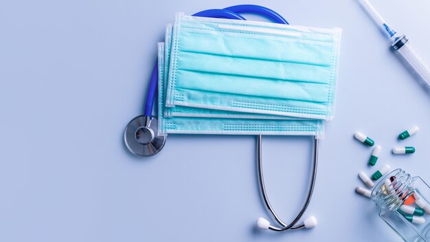 Mask with pills, stethoscope, syringe medical supply objects isolated on blue background, top view, flat lay, overhead shot, virus protection concept.