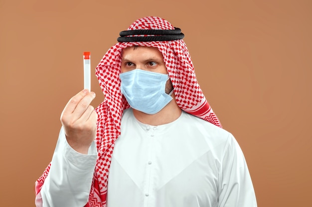 A masked Arab man holds a test tube in a national costume.