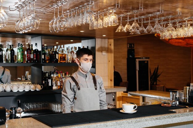 A masked barista exquisitely serves readymade coffee in a modern cafe during a pandemic Serving readymade coffee to a client in a cafe