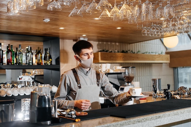 Бариста в маске изысканно подает готовый кофе в современном кафе во время пандемии Подача готового кофе клиенту в кафе