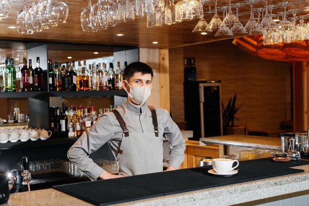 A masked barista exquisitely serves readymade coffee in a modern cafe during a pandemic Serving readymade coffee to a client in a cafe