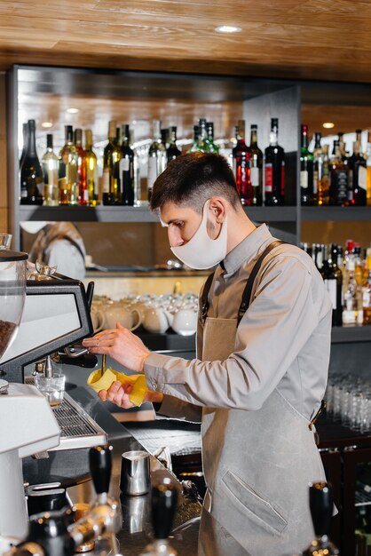 Un barista mascherato prepara un delizioso caffè al bar di una caffetteria. il lavoro di ristoranti e caffè durante la pandemia.