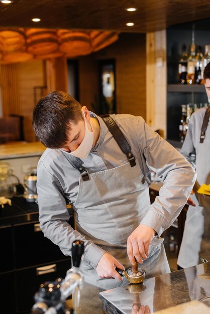 A masked barista prepares delicious coffee at the bar in a cafe. The work of restaurants and cafes during the pandemic.