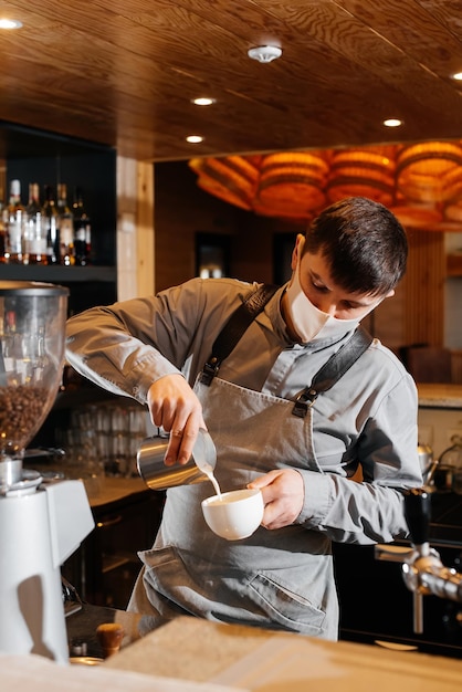 Un barista mascherato prepara uno squisito e delizioso caffè al bar di una caffetteria il lavoro di ristoranti e caffè durante la pandemia