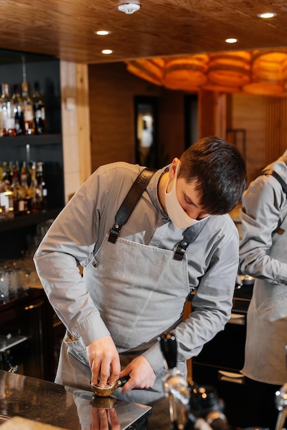 Un barista mascherato prepara uno squisito e delizioso caffè al bar di una caffetteria il lavoro di ristoranti e caffè durante la pandemia