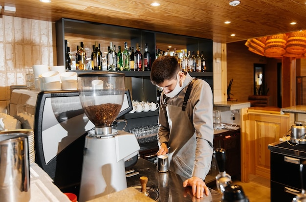 A masked barista prepares an exquisite delicious coffee at the bar in a coffee shop The work of restaurants and cafes during the pandemic