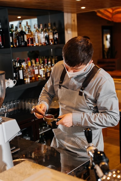 A masked barista prepares an exquisite delicious coffee at the bar in a coffee shop The work of restaurants and cafes during the pandemic