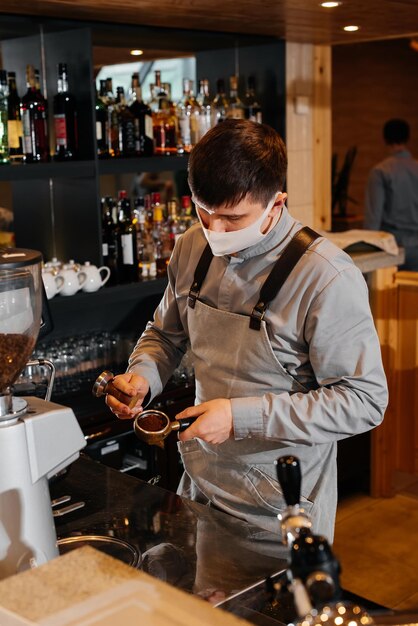 A masked barista prepares an exquisite delicious coffee at the bar in a coffee shop The work of restaurants and cafes during the pandemic