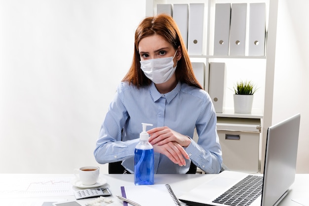 masked business woman washes her hands with gel in the workplace