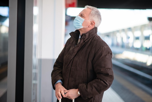 Masked businessman waiting for the train covid and coronavirus mobility concept