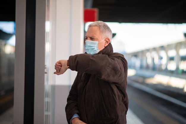 Masked businessman waiting for the train covid and coronavirus mobility concept