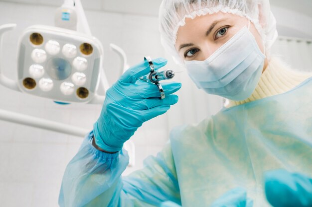 A masked dentist holds an injection syringe for a patient in the office.