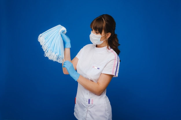 a masked doctor holds a set of masks on a blue background