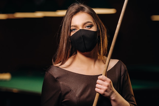 Masked girl in a pool club with a cue in her hands