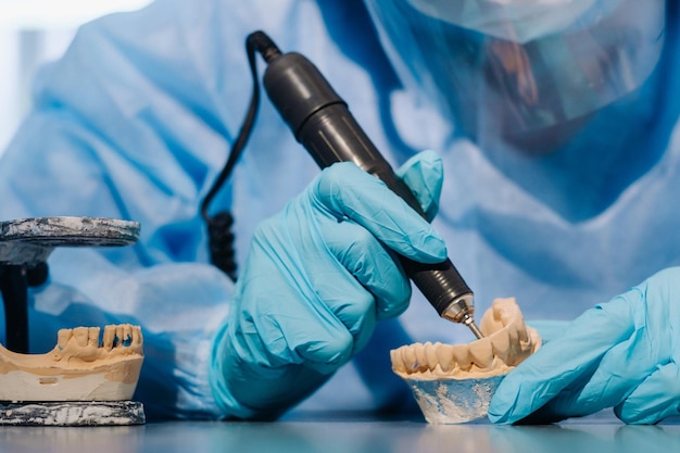 A masked and gloved dental technician works on a prosthetic tooth in his lab