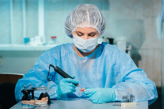 マスクをして手袋をはめた歯科技工士が、自分の研究室で義歯に取り組んでいます。