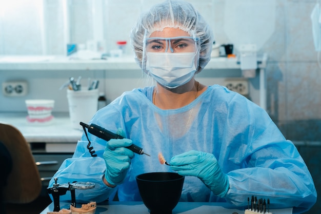 Зубной техник в маске и перчатках работает над протезом зуба в своей лаборатории