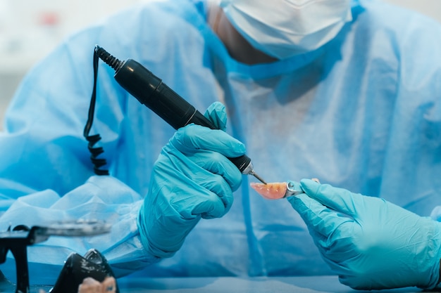 A masked and gloved dental technician works on a prosthetic tooth in his lab