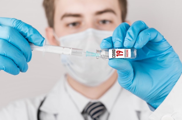 A masked male doctor injects the COVID-19 vaccine with a syringe. Health care and medical concept.