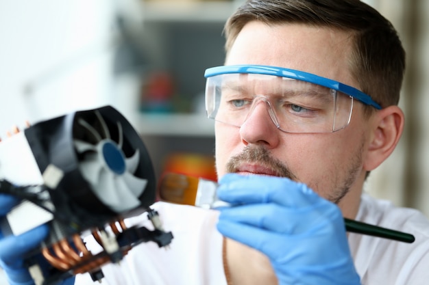 Masked man repairs and dusts a computer part