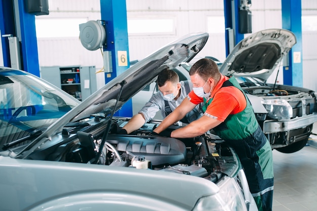 A masked mechanic checks the car at the service station