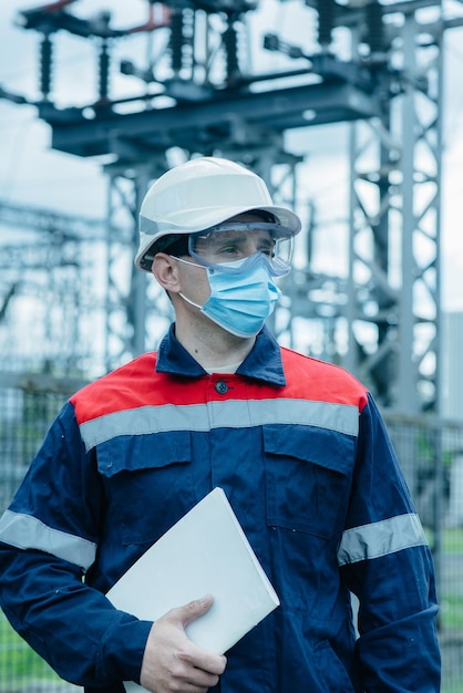 A masked power engineer during a pandemic inspects the modern equipment of an electrical substation before commissioning Energy and industry Scheduled repair of electrical equipment